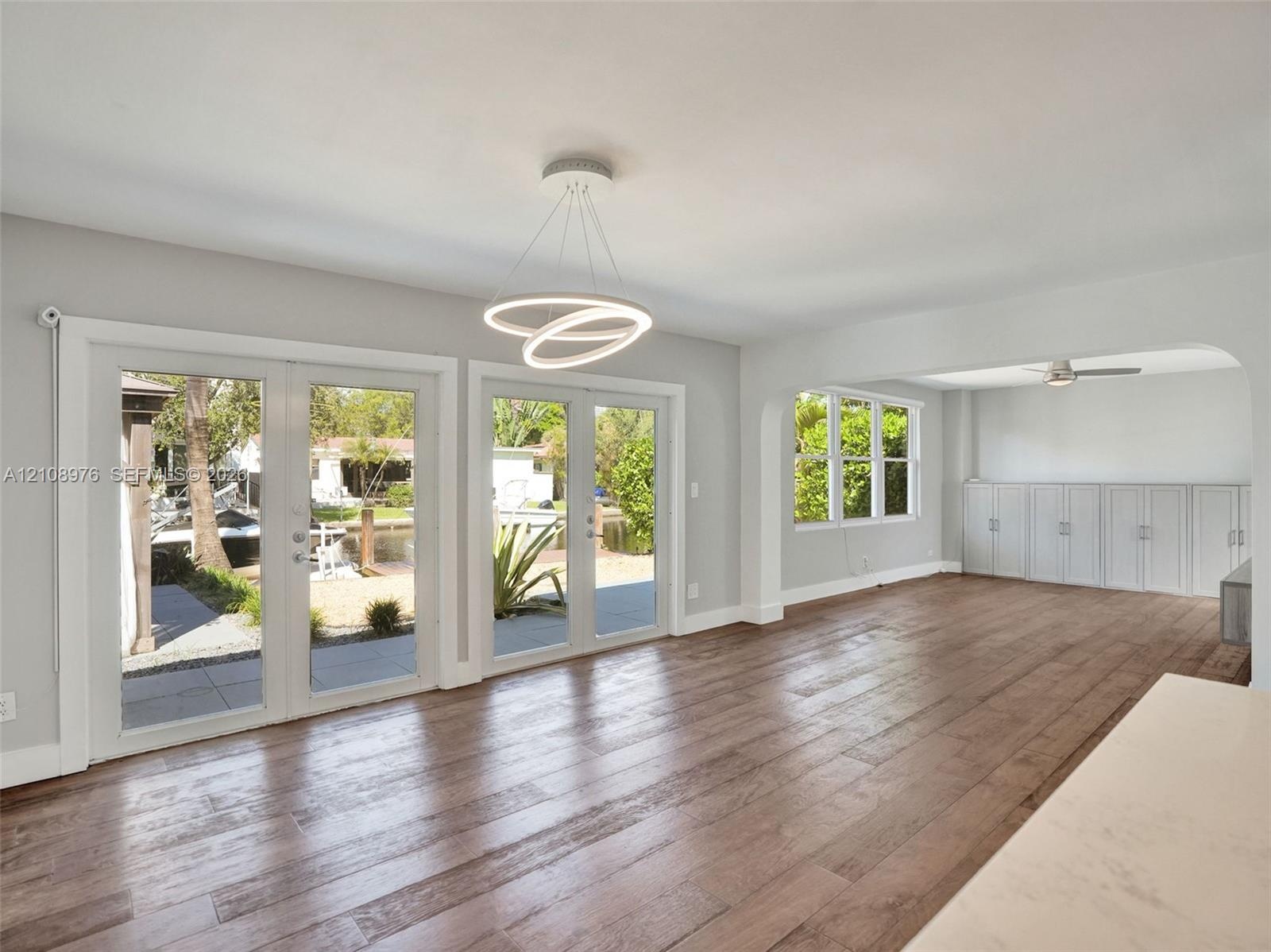 Living space featuring wood-finish flooring, dual sets of French doors, an integrated circular LED light fixture, and custom built-in cabinetry with a