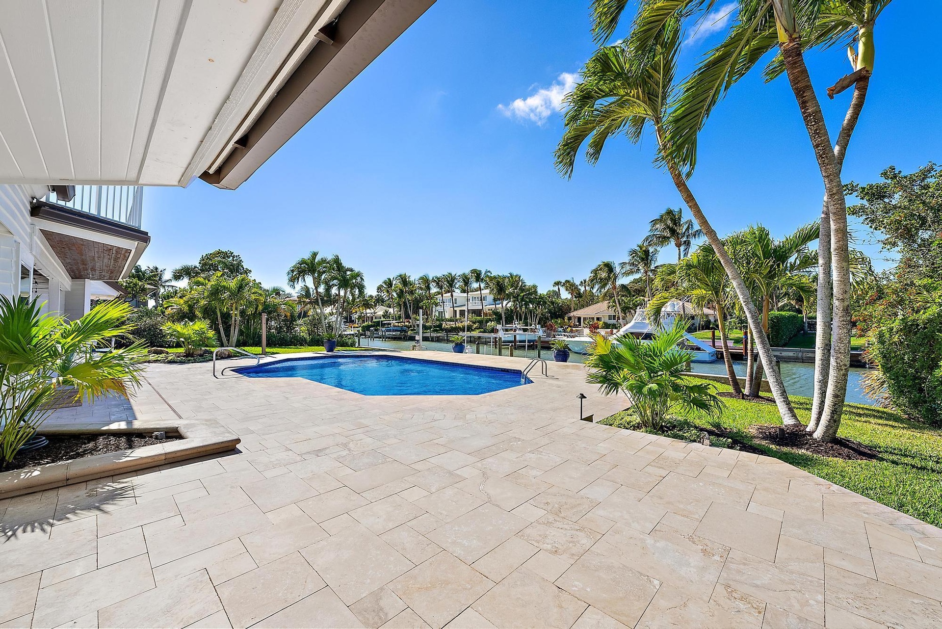 Waterfront patio featuring stone paver hardscaping, a custom-shaped swimming pool, built-in metal pool railings, and mature palm landscaping