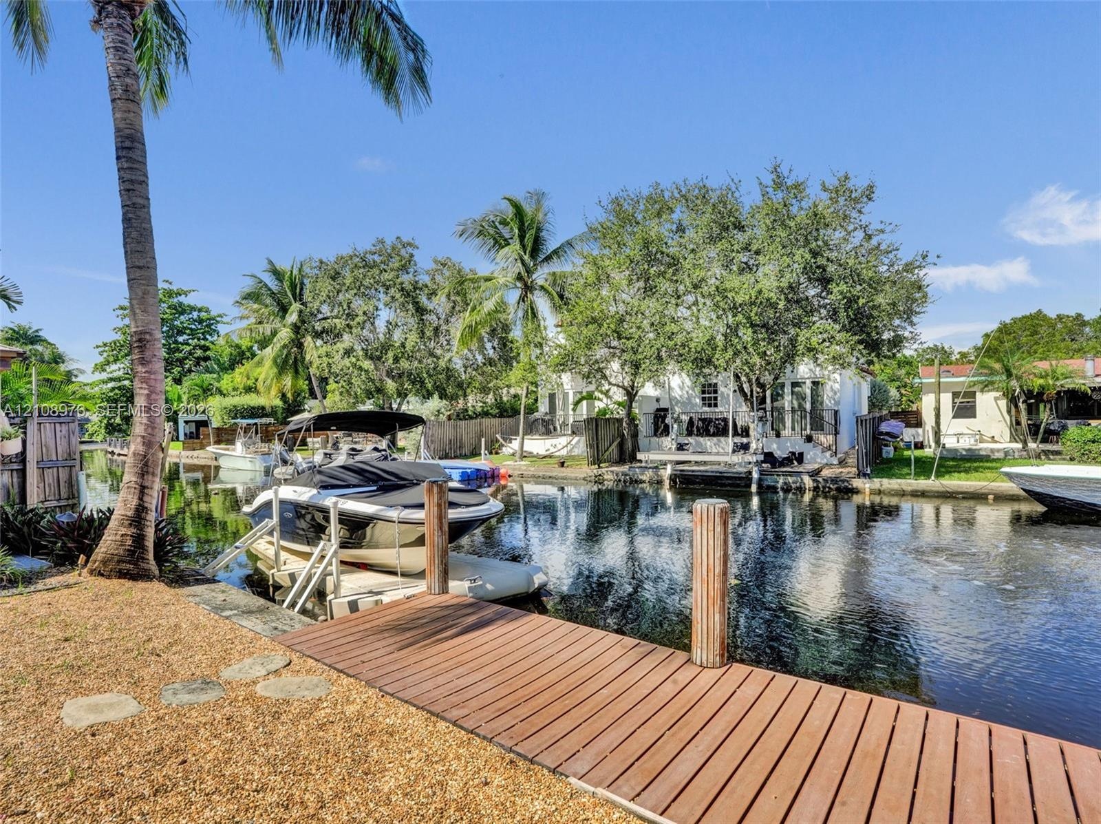 Waterfront canal property featuring a private wood-plank dock, boat lift, gravel landscaping, and mature palm trees