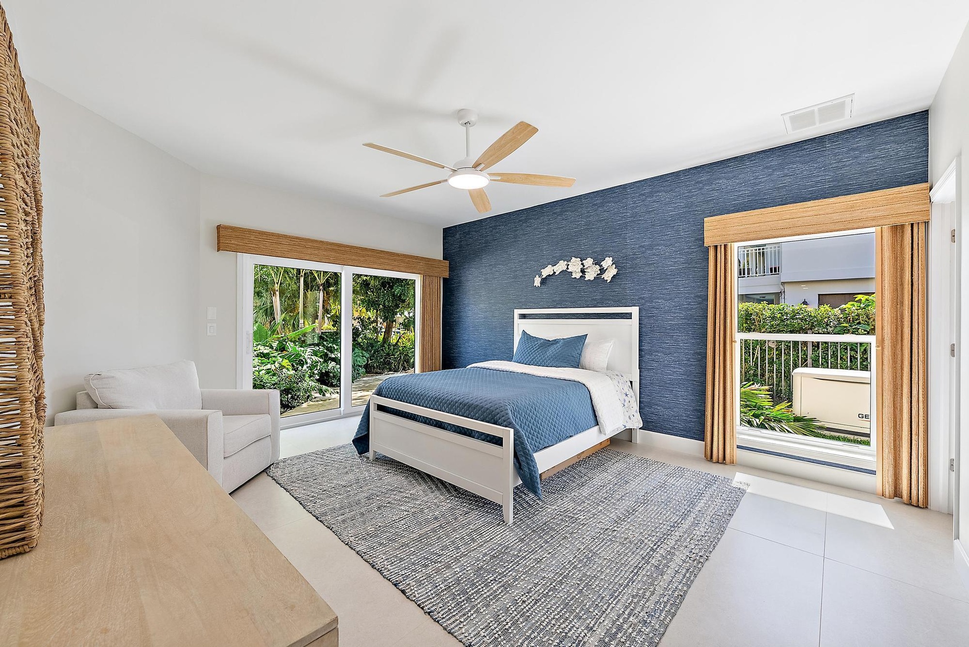 Textured navy blue accent wall, large-format tile flooring, ceiling fan with light fixture, and two sets of sliding glass doors featuring bamboo-finis
