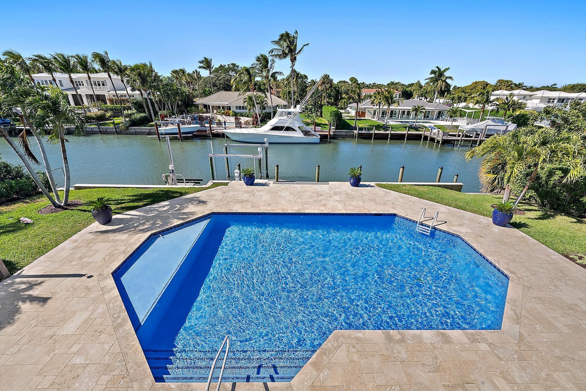 Waterfront property featuring a private boat dock, in-ground swimming pool, stone-paver deck, and manicured lawn