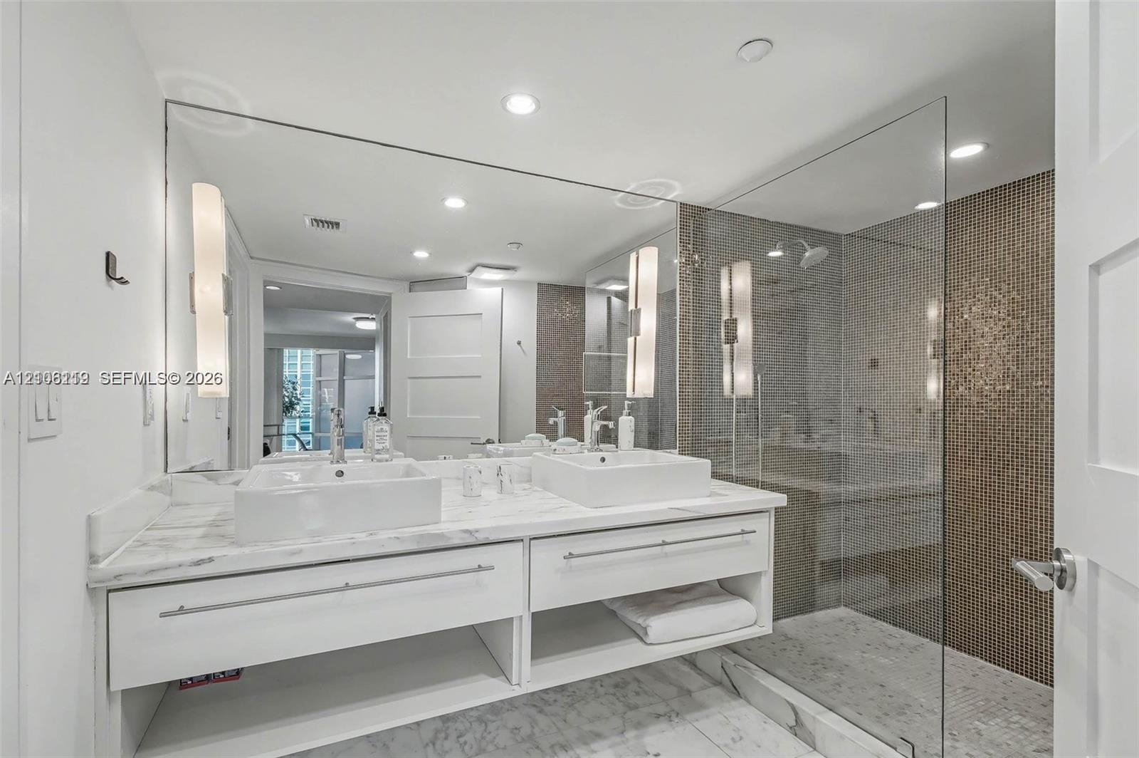 Floating vanity with dual rectangular vessel sinks, expansive wall-to-wall mirror, glass-enclosed shower with mosaic wall tiling, and stone flooring