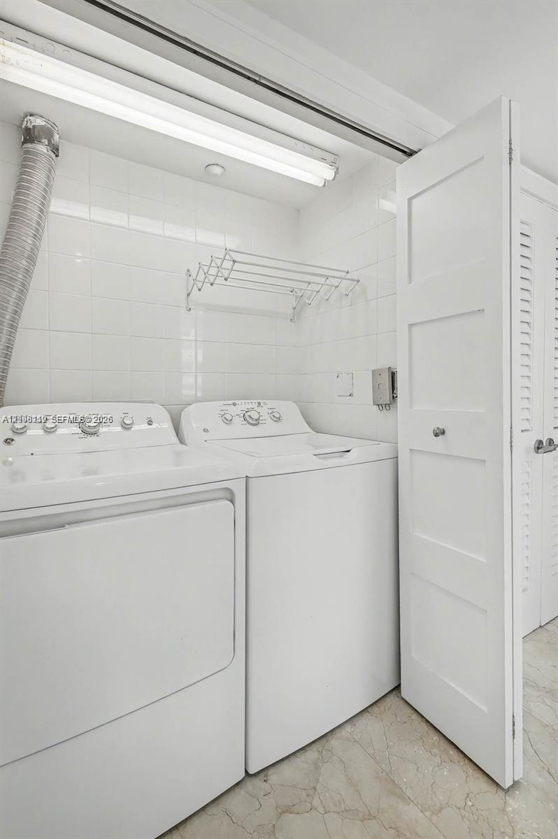 Laundry area featuring white ceramic wall tiling, stone-finish flooring, built-in wall-mounted drying rack, and white shaker-style doors