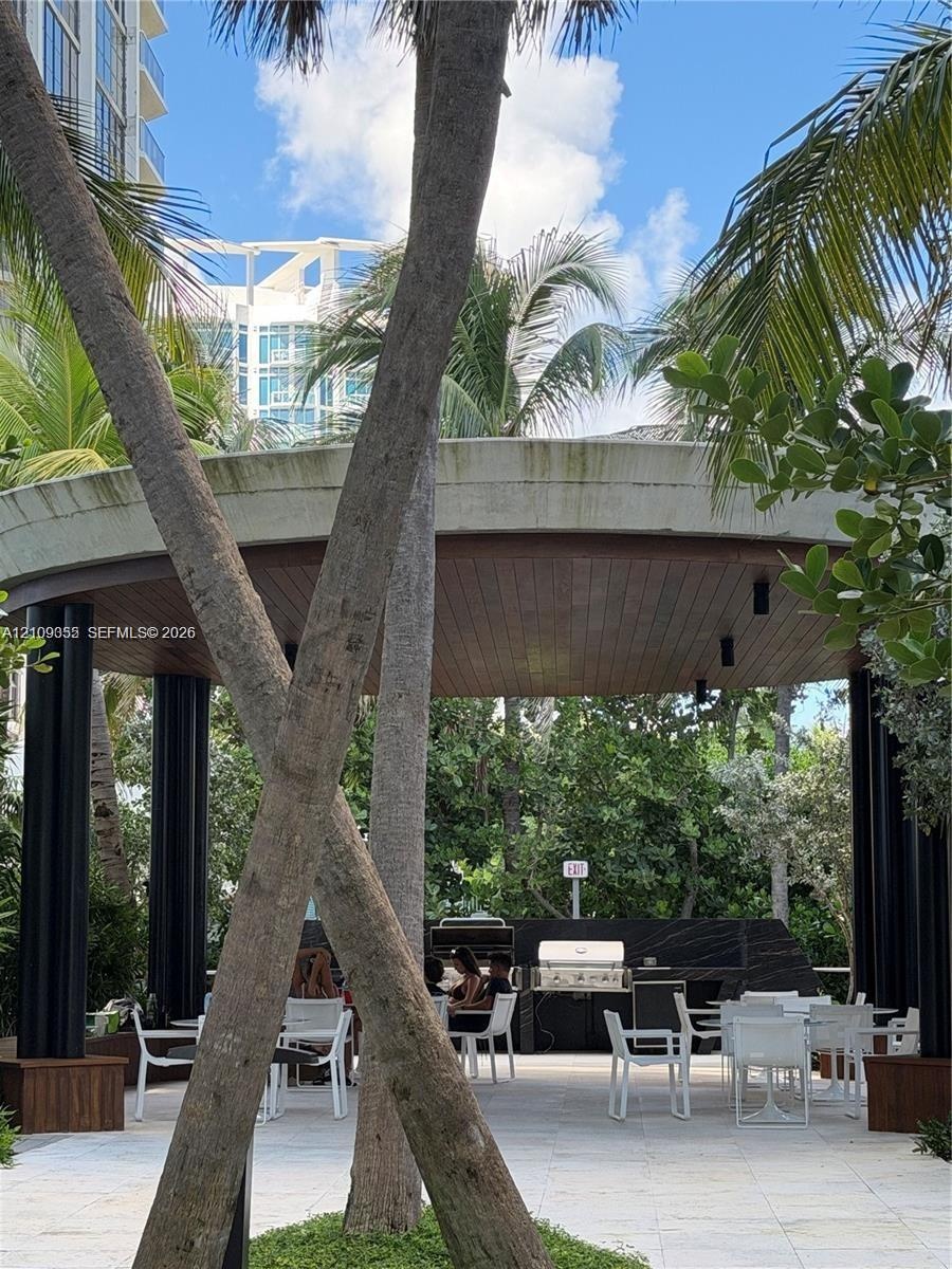 Outdoor pavilion featuring a circular concrete roof, wood-plank ceiling, black support columns, built-in stone-finish grill station, and stone-tile pa