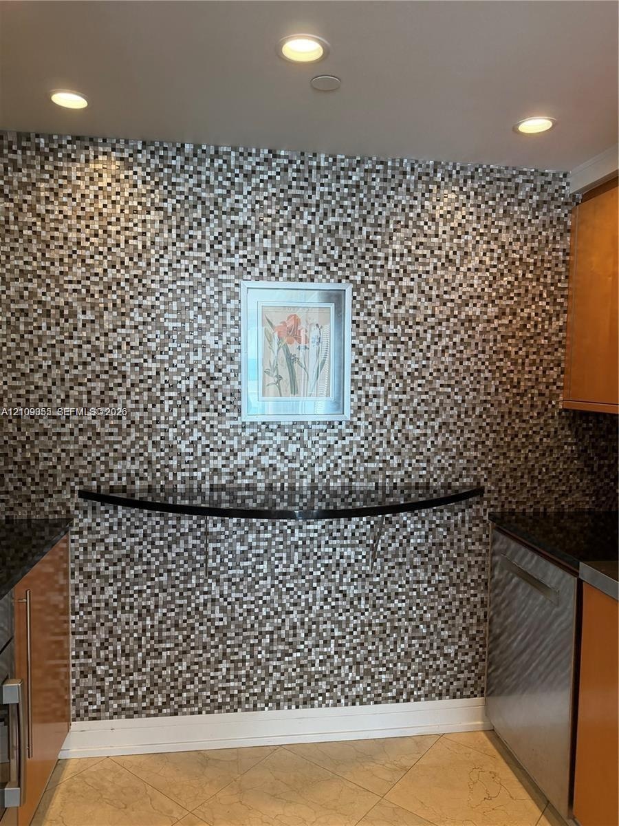 Multi-tonal mosaic tile wall, integrated black stone counter, recessed ceiling lighting, and polished wood-finish cabinetry