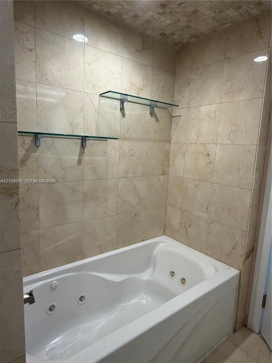 Jetted bathtub featuring full-height natural stone wall tiling and two integrated glass shelving units