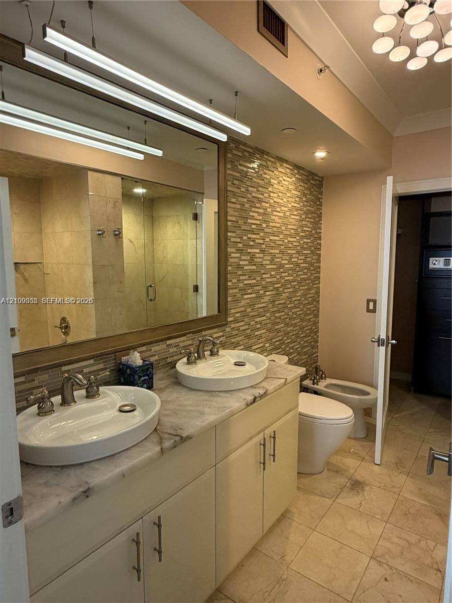 Double vanity with oval vessel sinks, stone countertop, mosaic tile backsplash, and stone tile flooring