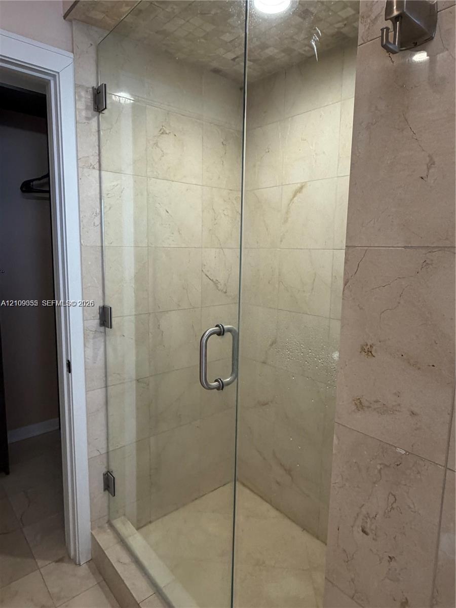 Walk-in shower featuring large-format tile surround, frameless glass door, metallic hardware, and integrated ceiling lighting