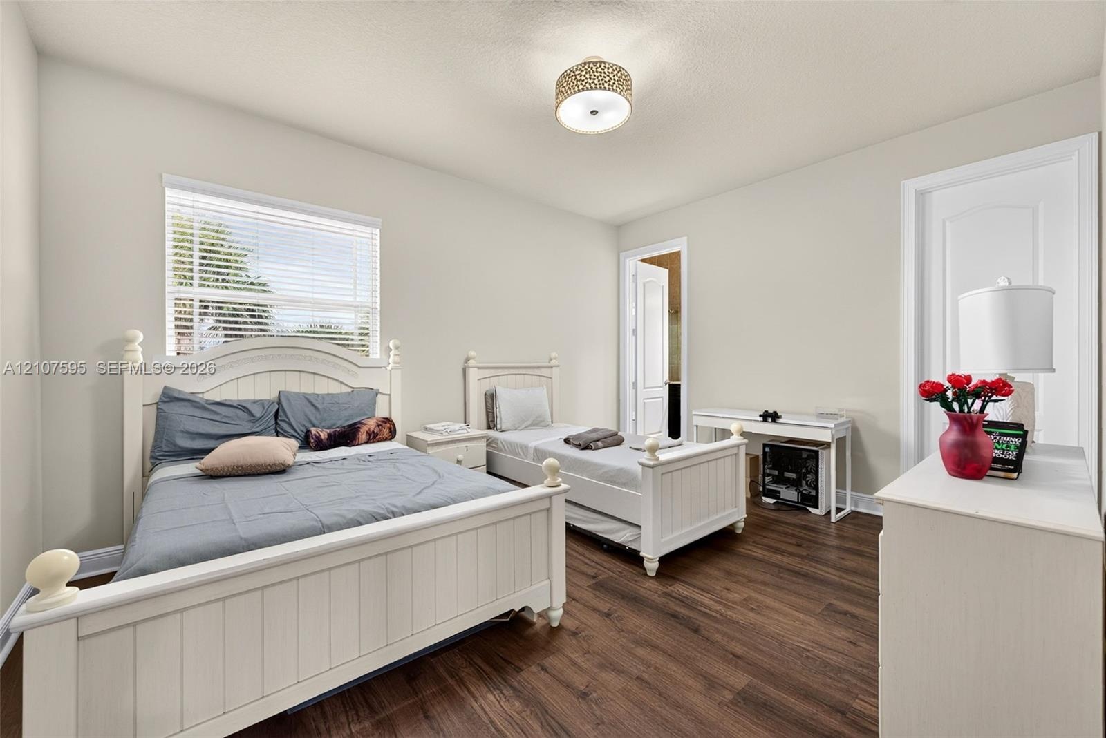 Bedroom featuring wood-finish flooring, a neutral color palette, natural light via horizontal blinds, and a circular drum flush-mount light fixture