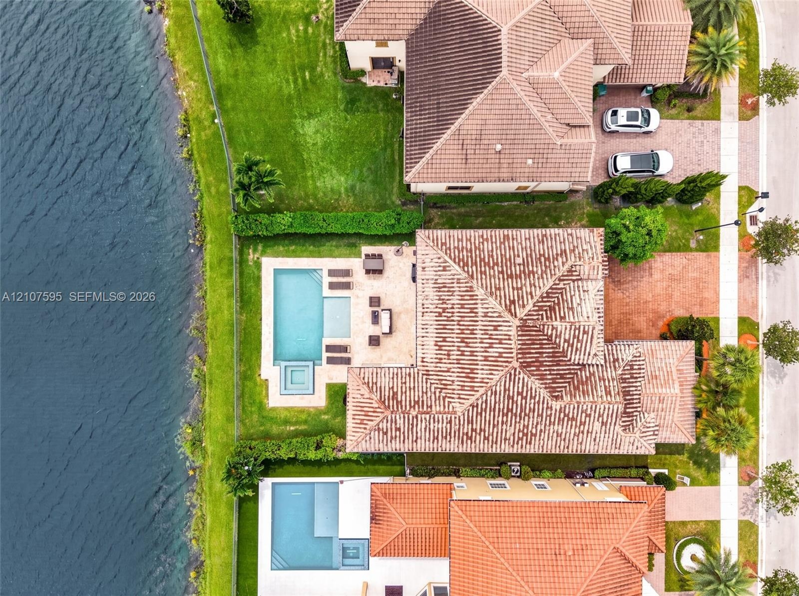 Waterfront property featuring a paver patio, a custom swimming pool with an integrated spa, and a tiled roof