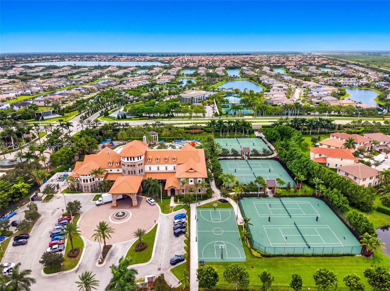 Mediterranean-style estate featuring a multi-story clubhouse, circular motor court with central fountain, multiple tennis courts, and a basketball cou