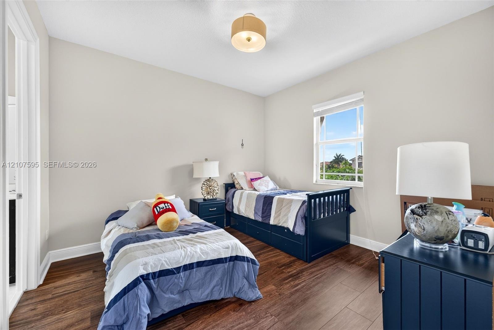 Neutral-toned walls, wood-finish flooring, a single-hung window with a roller shade, and a drum-style ceiling light fixture
