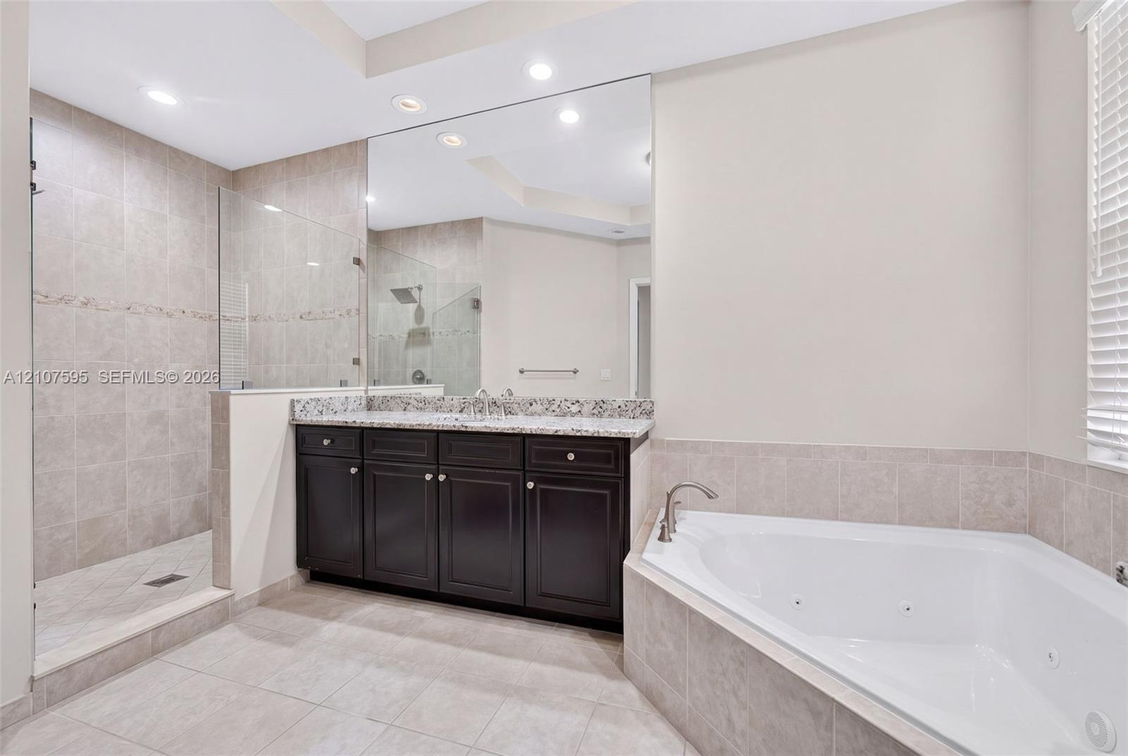 Bathroom featuring a dark wood vanity with a stone countertop, an oversized wall mirror, a corner jetted soaking tub, and a glass-enclosed walk-in sho