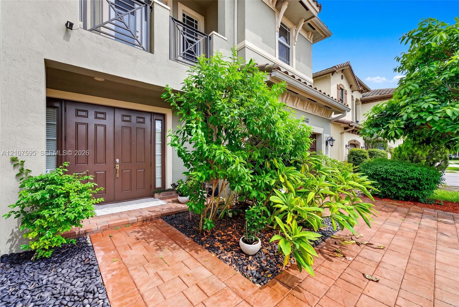 Stucco exterior featuring a double-door entrance, paver walkway, balcony with metal railing, and decorative brackets