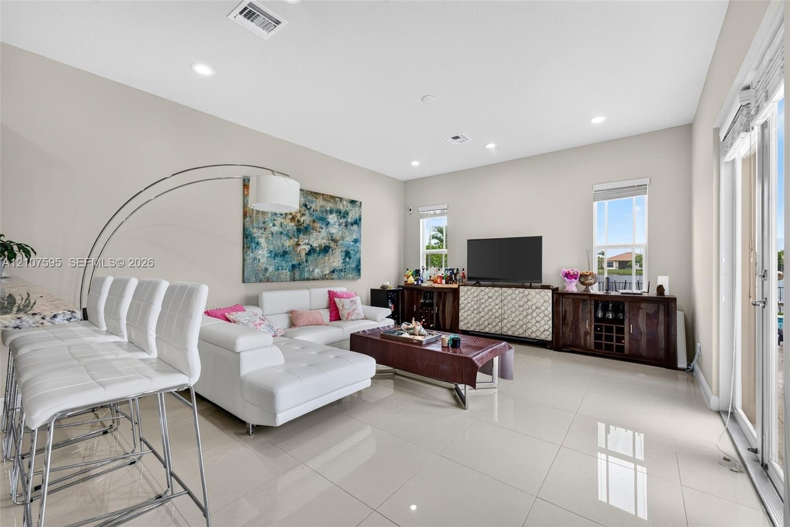 Open-concept living space featuring high ceilings, neutral wall tones, large-format tile flooring, recessed lighting, and sliding glass doors