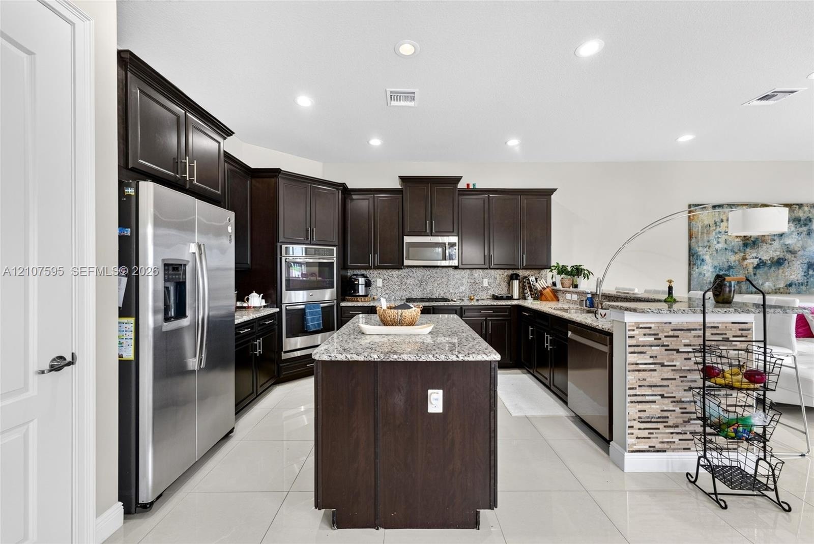 Kitchen featuring dark cabinetry, stone-surface countertops, central island, stainless steel appliances, and large-format tile flooring