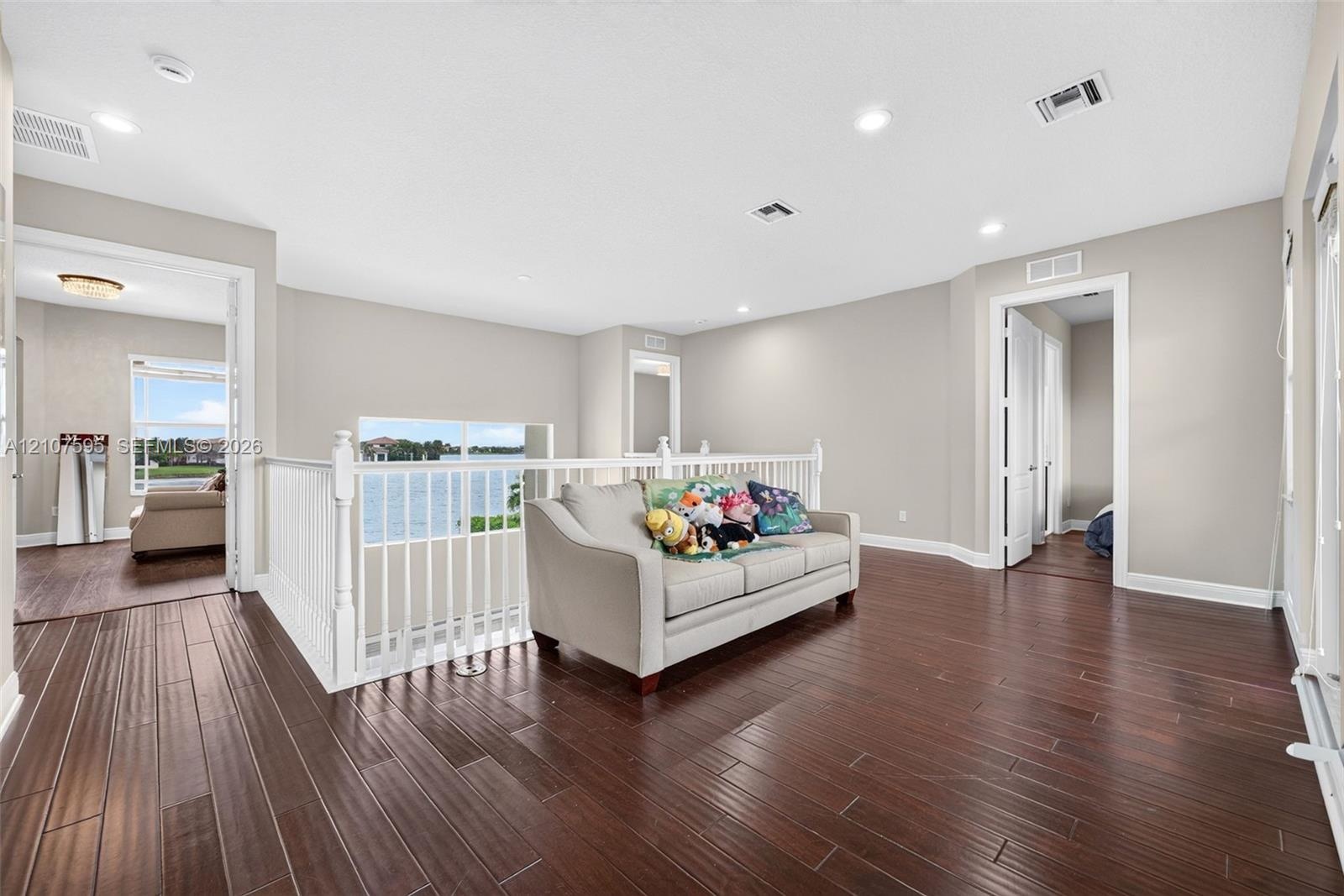 Open loft area featuring wood-finish flooring, recessed lighting, and a white balustrade railing overlooking the water