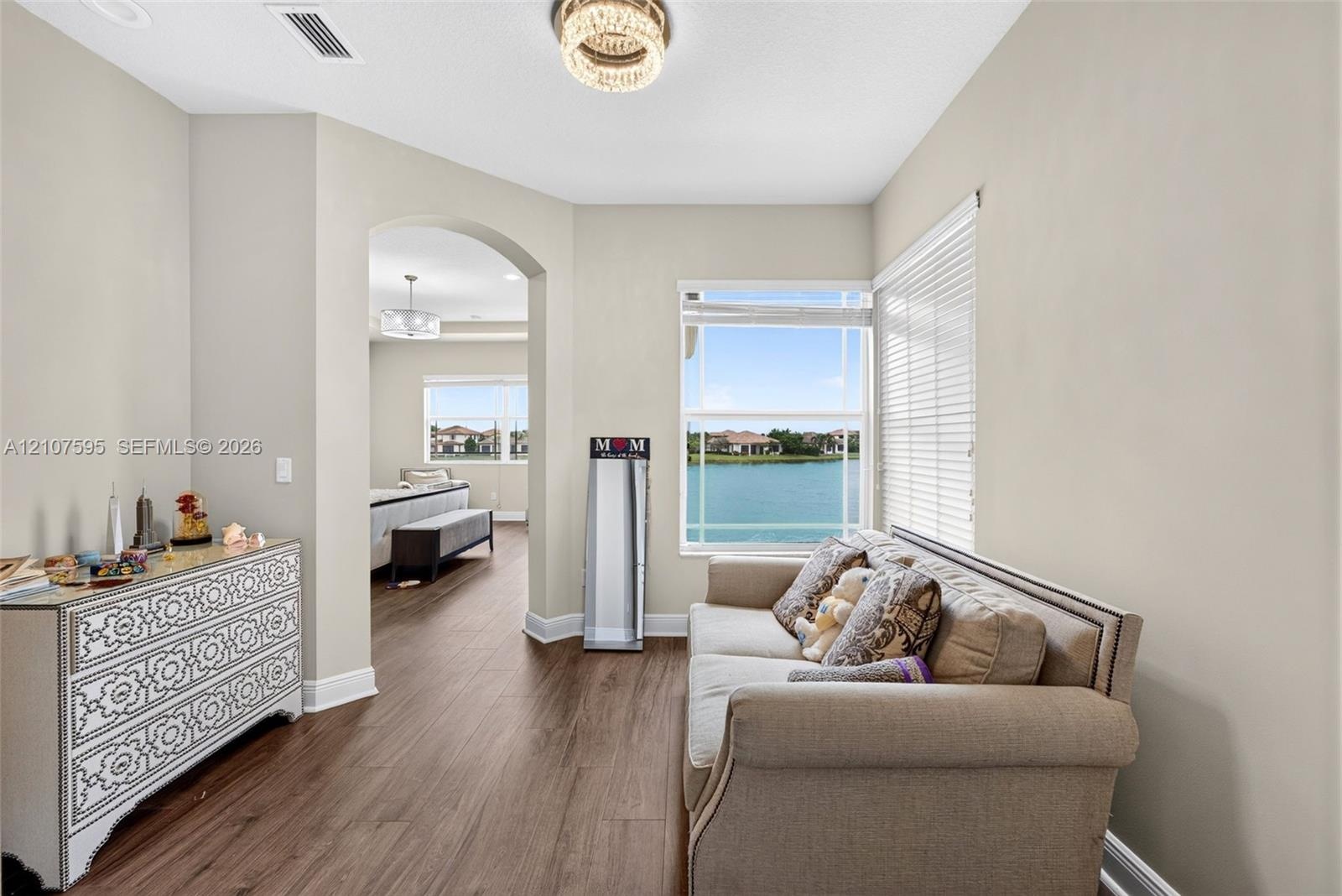 Wood-finish flooring, arched entryway, large window with water scenery, and decorative drum-style ceiling lighting