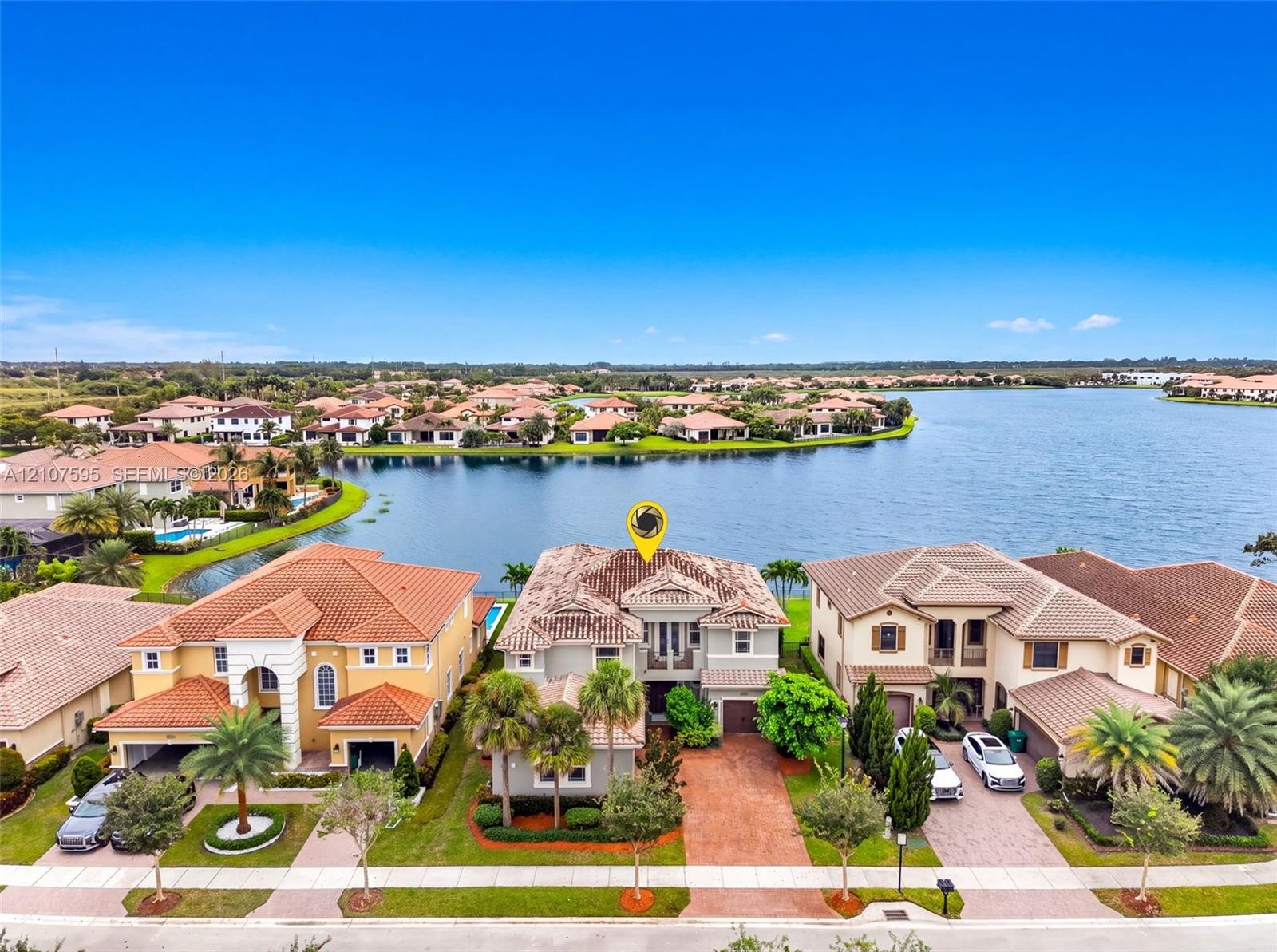Waterfront property featuring a multi-story exterior with a tile roof, paved driveway, and mature landscaping