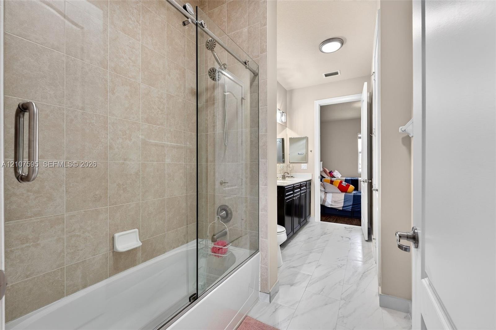 Bathroom featuring a tub-shower combination with floor-to-ceiling neutral tile surround and glass sliding doors, dark wood-finish cabinetry, stone-sty