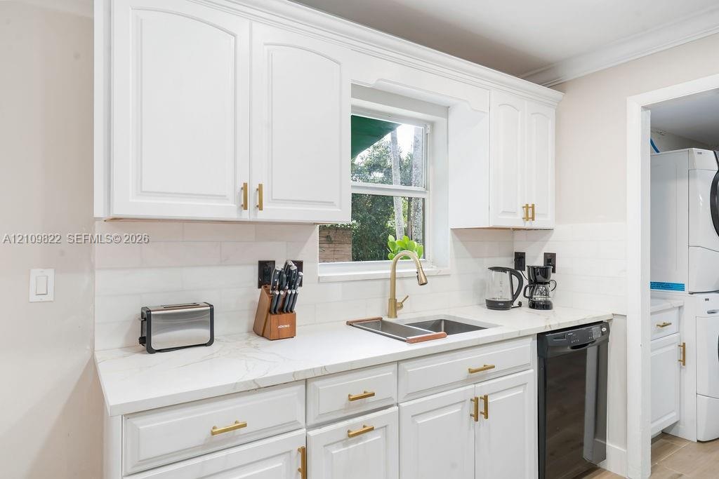 Kitchen featuring white cabinetry, light-toned stone-finish countertops, brass-toned hardware, subway tile backsplash, and an undermount sink with a m