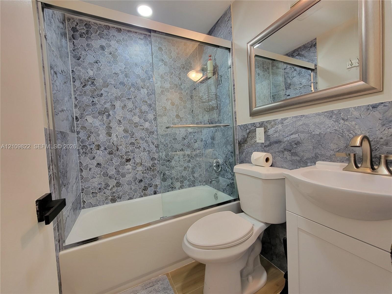 Full bathroom featuring a tub-shower combination with glass sliding doors, honeycomb-patterned tile surround, vanity with an integrated basin, brushed
