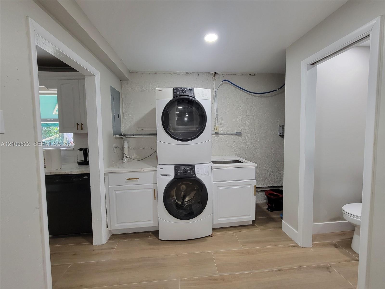 Utility area featuring white shaker-style cabinetry, an integrated sink with a countertop, and wood-finish tile flooring