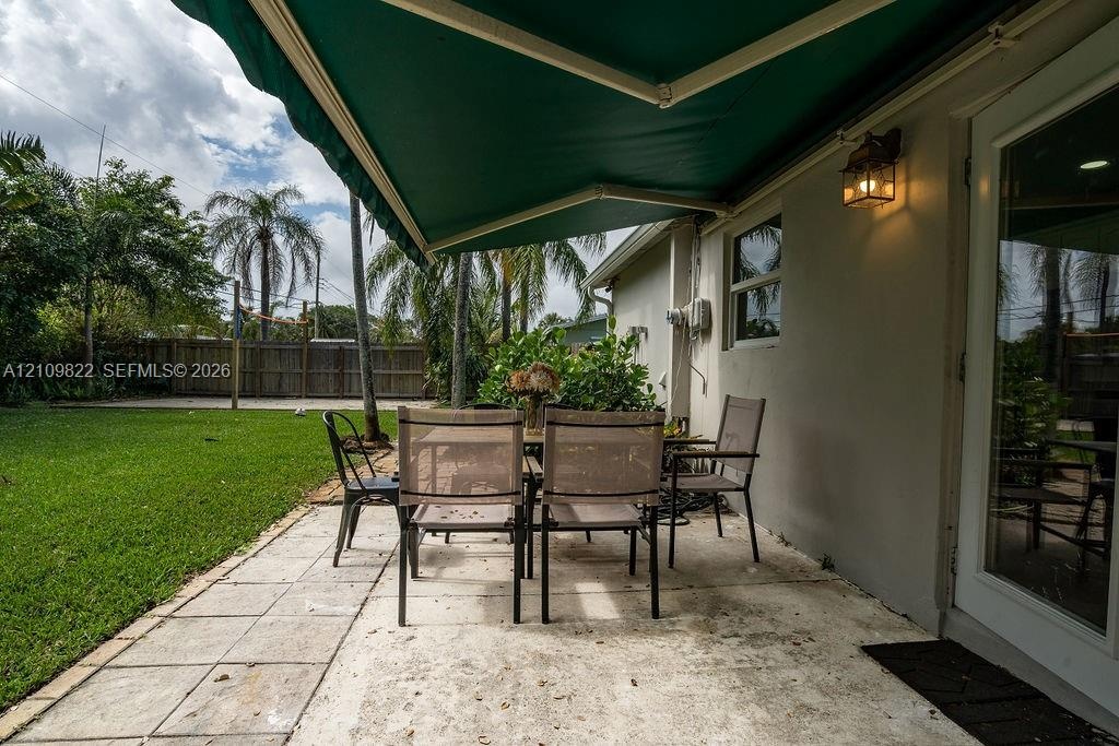 Backyard patio featuring concrete pavers, a retractable green awning, attached exterior wall-mounted lighting, and a fenced grass lawn