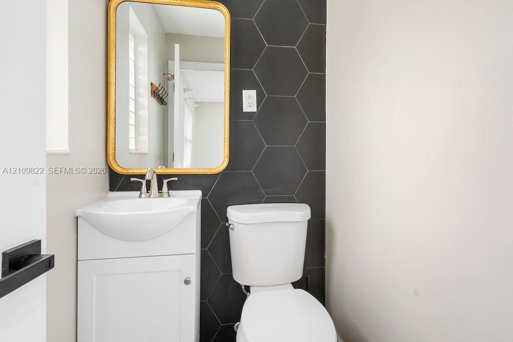 Wall-mounted sink with brushed nickel faucet, matte black hexagonal tile accent wall, and integrated cabinetry