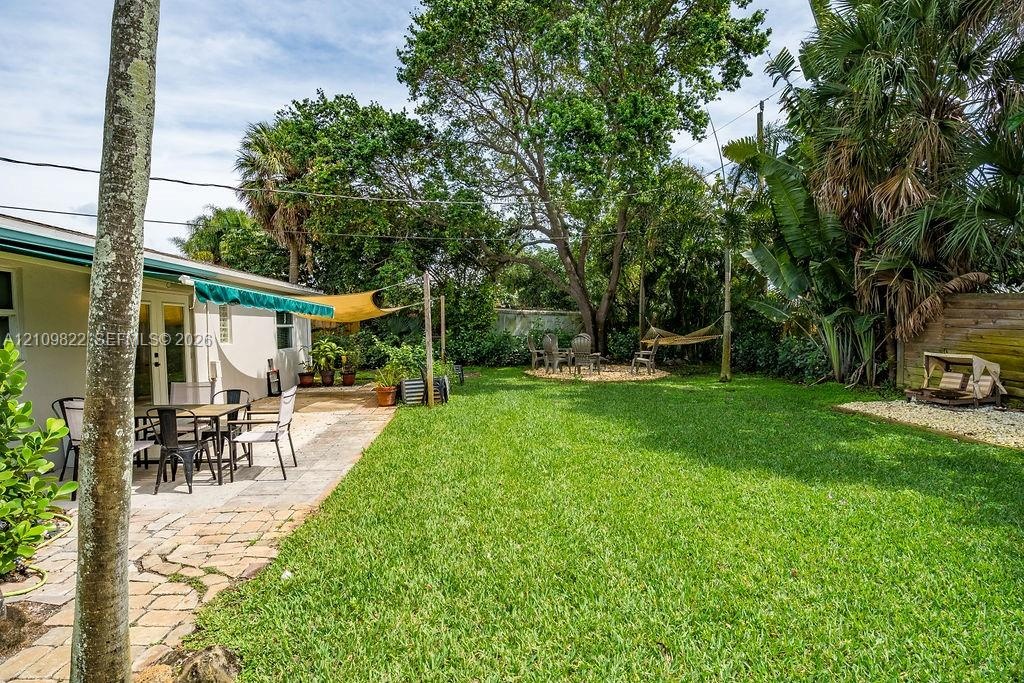 Backyard featuring a paved stone patio, mature canopy trees, lush lawn, and palm-lined perimeter
