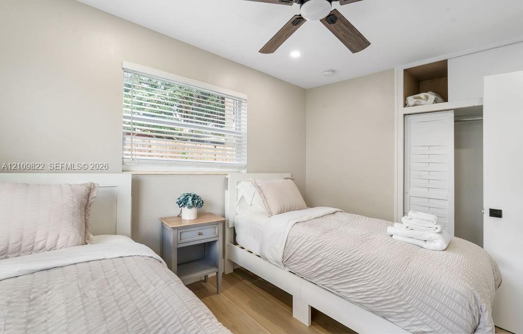 Neutral-toned room featuring wood-finish flooring, a ceiling fan with integrated lighting, a window with horizontal blinds, and a built-in closet with