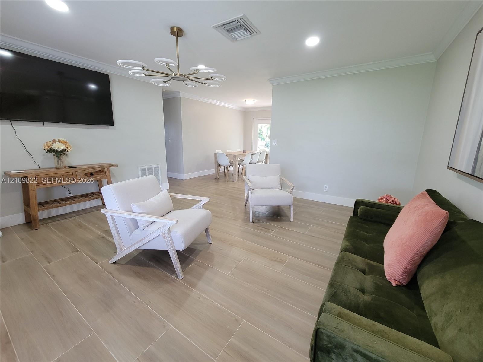 Open-concept living space featuring wood-finish tile flooring, crown molding, recessed lighting, and a multi-arm modern light fixture