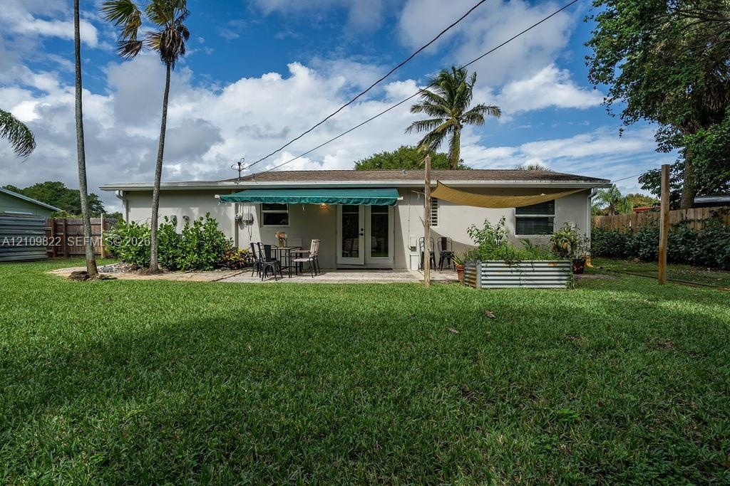 Expansive backyard featuring a manicured lawn, paved patio, retractable awning, mature palms, and metal raised garden beds