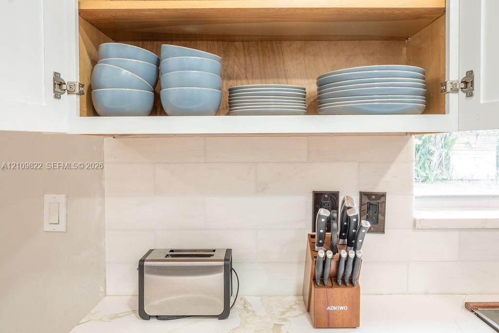 Upper cabinetry featuring natural wood-tone interior shelving, stone-composite countertop, and a horizontal-set rectangular tile backsplash