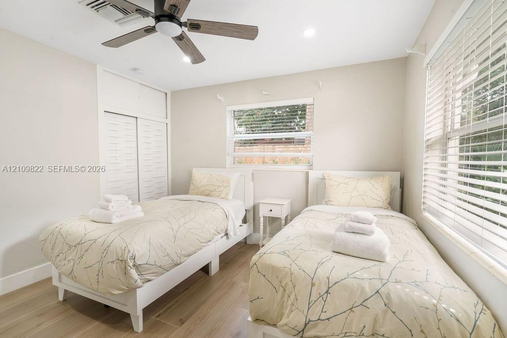 Neutral-toned interior featuring wood-finish flooring, a multi-blade ceiling fan, recessed lighting, and dual-window installations with horizontal bli