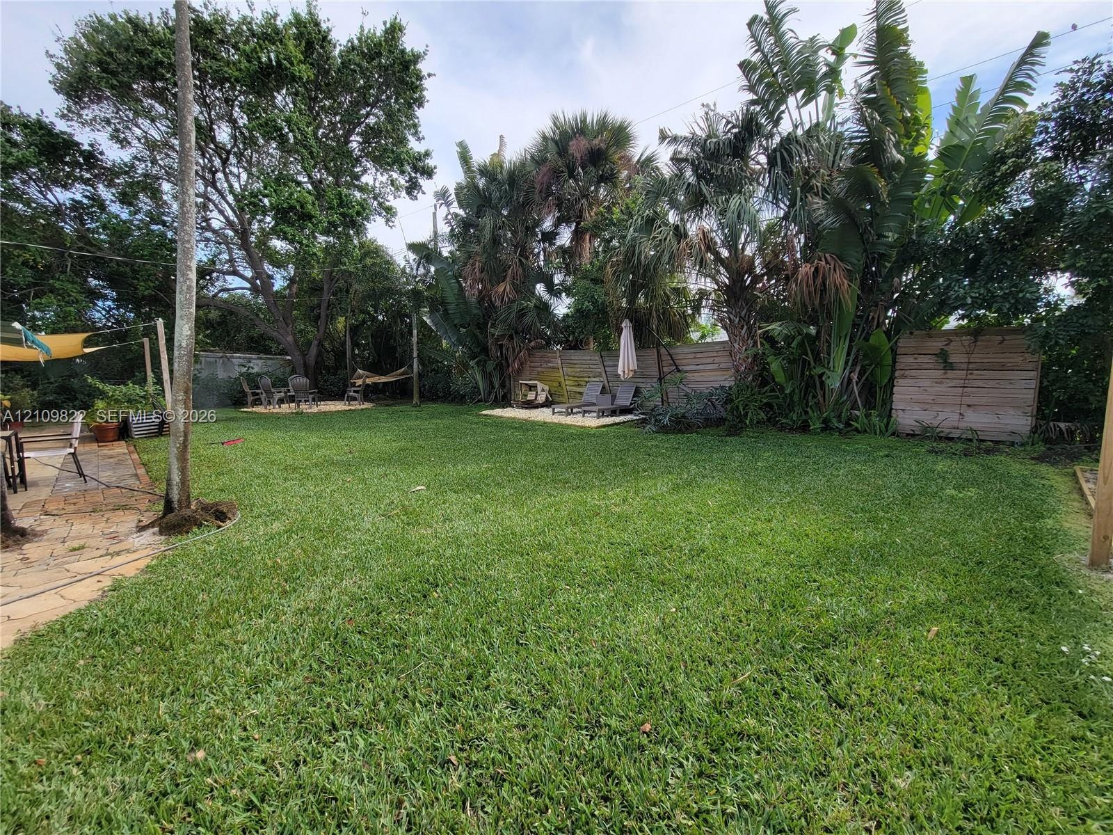 Expansive backyard featuring a natural grass lawn, mature palm trees, flagstone patio, and perimeter wood fencing