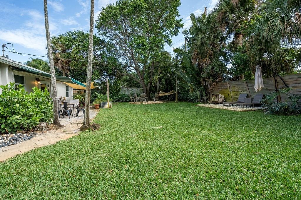 Backyard featuring a manicured lawn, flagstone pathway, mature shade trees, palm landscaping, and a gravel hardscape area