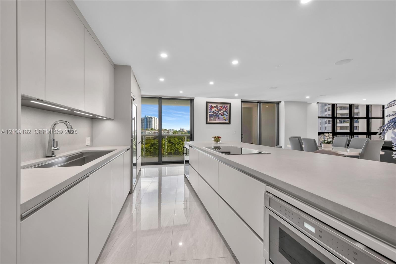 Kitchen featuring flat-panel cabinetry, a quartz waterfall-edge island with an integrated cooktop, stone-finish flooring, a stainless steel wine refri