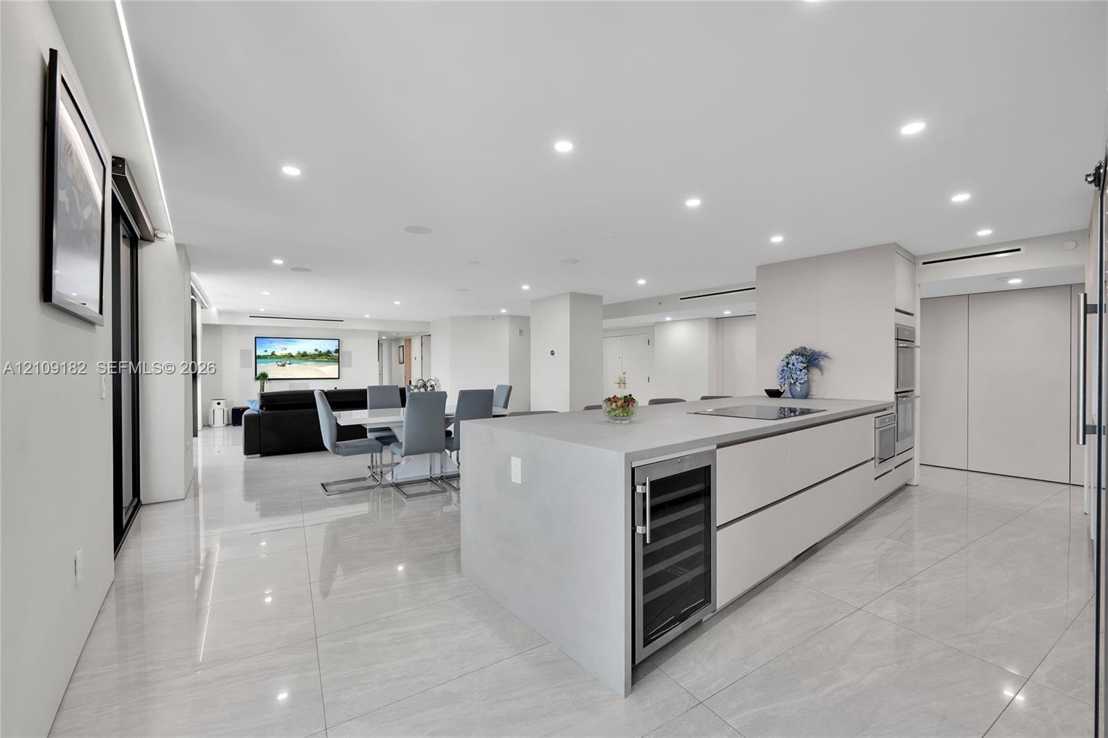 Open kitchen featuring matte-finish cabinetry, a large central island with a solid-surface countertop, integrated cooktop, polished tile flooring, and
