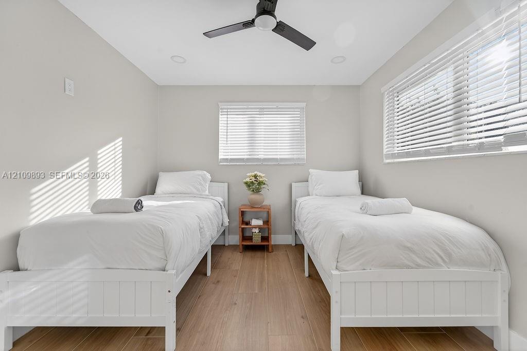 Neutral-toned walls paired with wood-finish flooring, featuring recessed ceiling lighting, a matte black ceiling fan, and horizontal window blinds