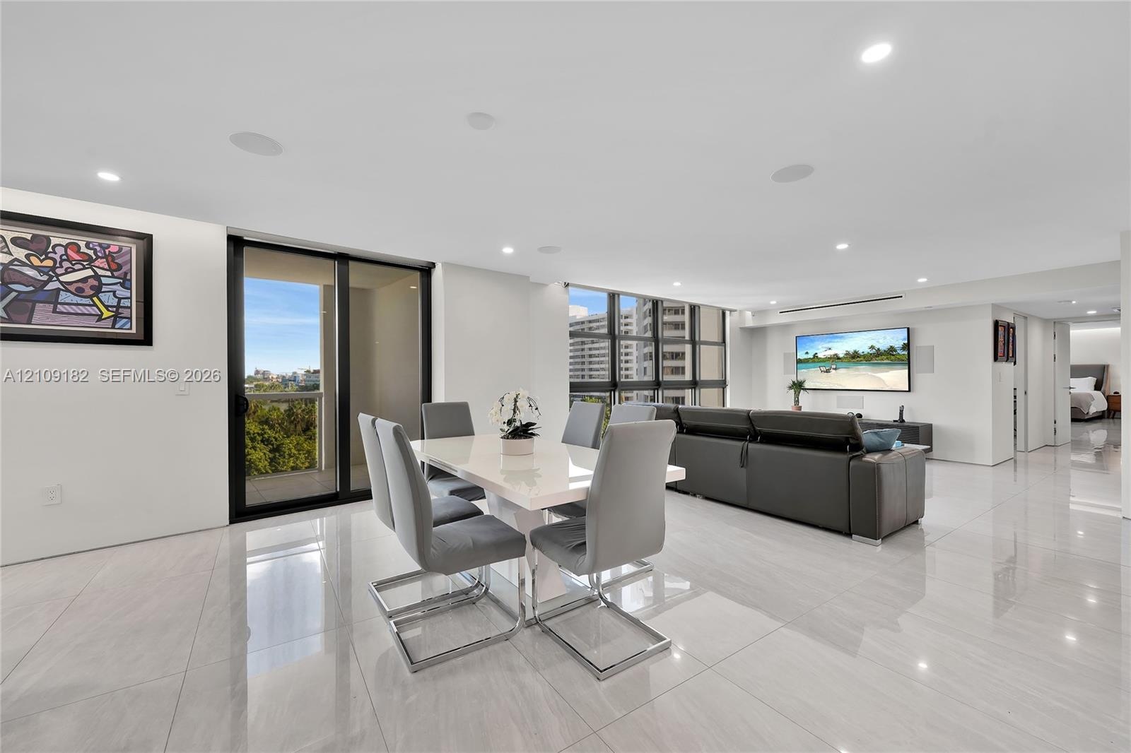 Open-concept interior featuring large-format tile flooring, floor-to-ceiling windows, recessed lighting, and a sliding glass door to an exterior balco