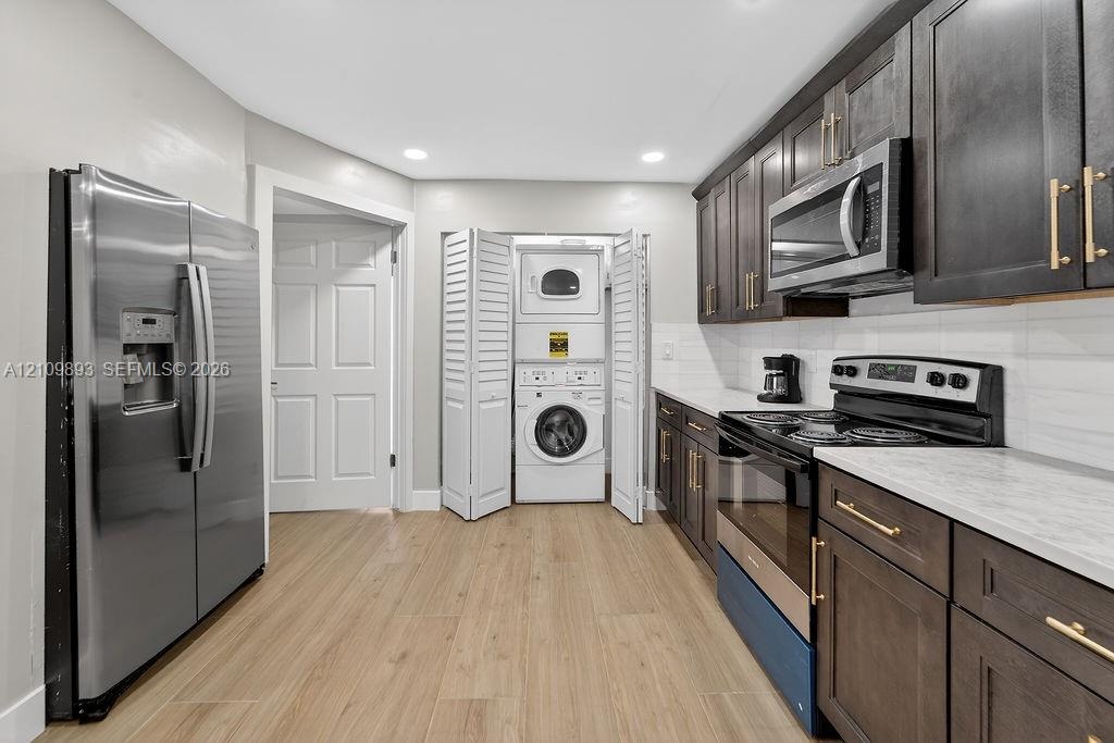 Kitchen featuring dark-stained shaker cabinetry, stainless steel appliances, light-toned stone-finish countertops, wood-finish flooring, and an integr