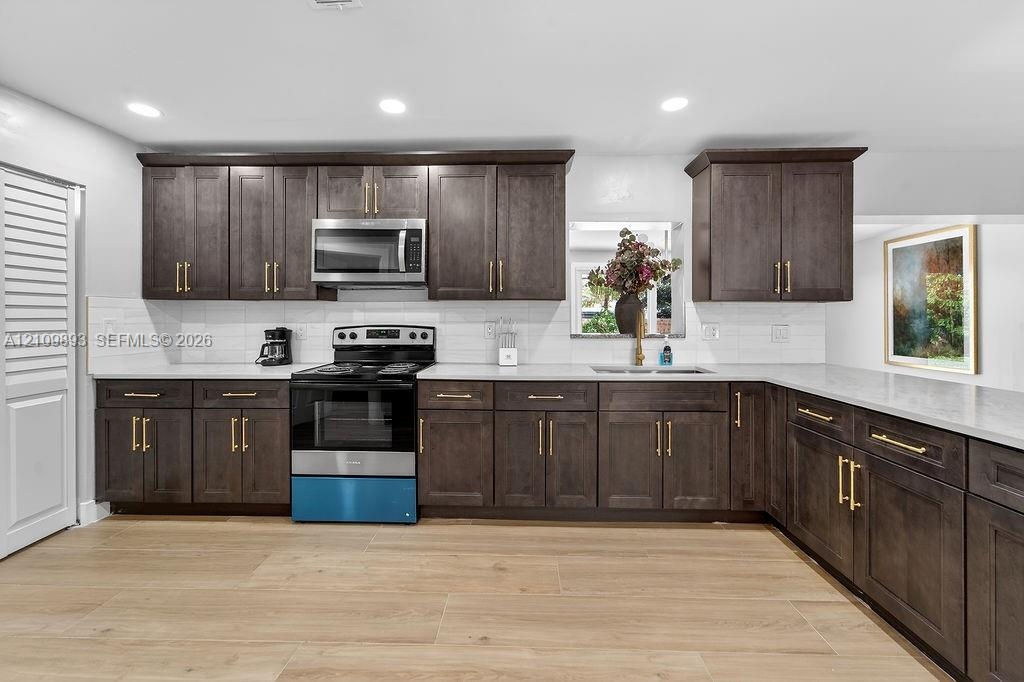 Kitchen featuring dark-finish cabinetry with brass-tone hardware, stone countertops, white subway tile backsplash, stainless steel appliances, and woo