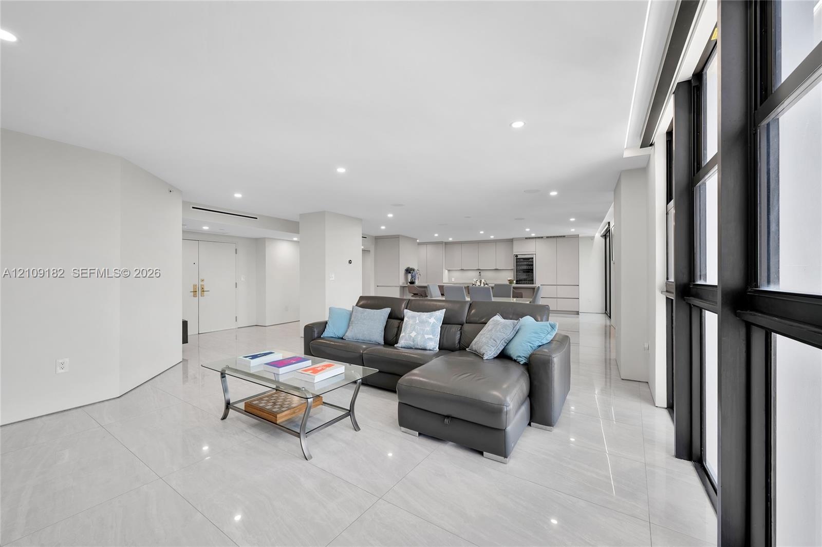 Open-concept floor plan featuring large-format polished tile flooring, floor-to-ceiling windows with dark framing, recessed lighting, and built-in min