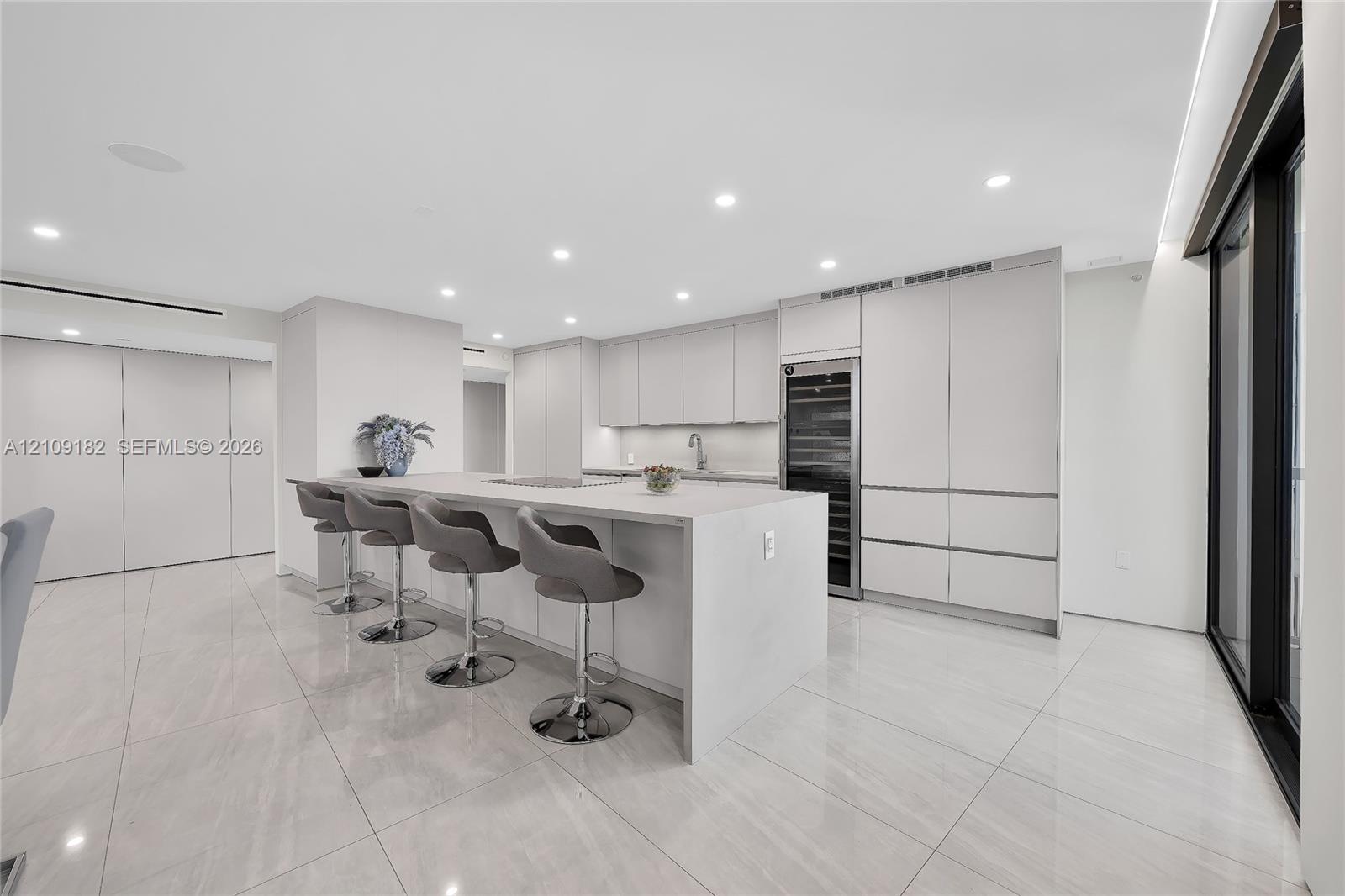 Open kitchen featuring flat-panel cabinetry, a central island with a solid-surface countertop, built-in wine refrigeration, and polished stone-finish 