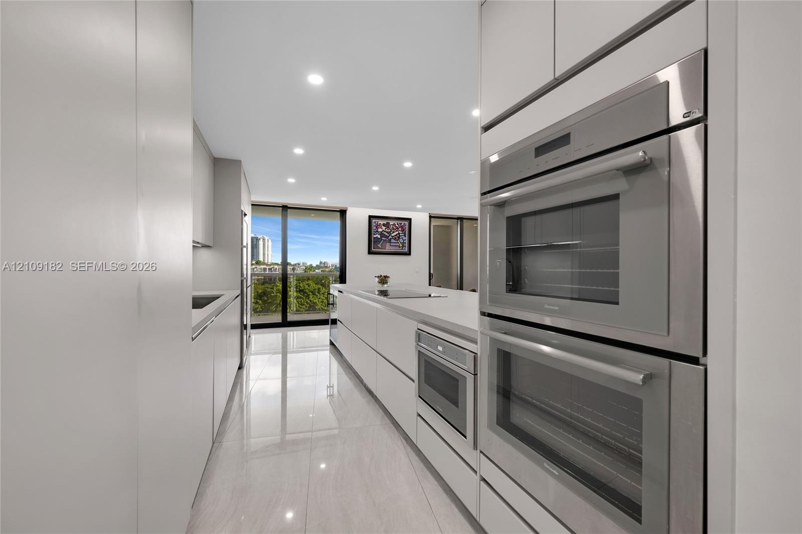 Open kitchen featuring flat-panel cabinetry, light-toned waterfall countertop, built-in wine refrigeration, large-format tile flooring, and floor-to-c