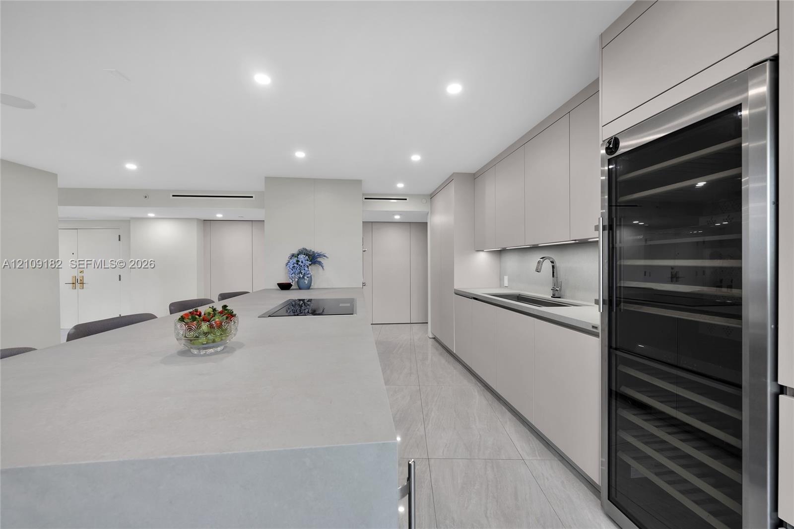 Kitchen island featuring a flat-panel cabinetry base, integrated under-counter beverage refrigerator, and an inset electric cooktop with a neutral-ton