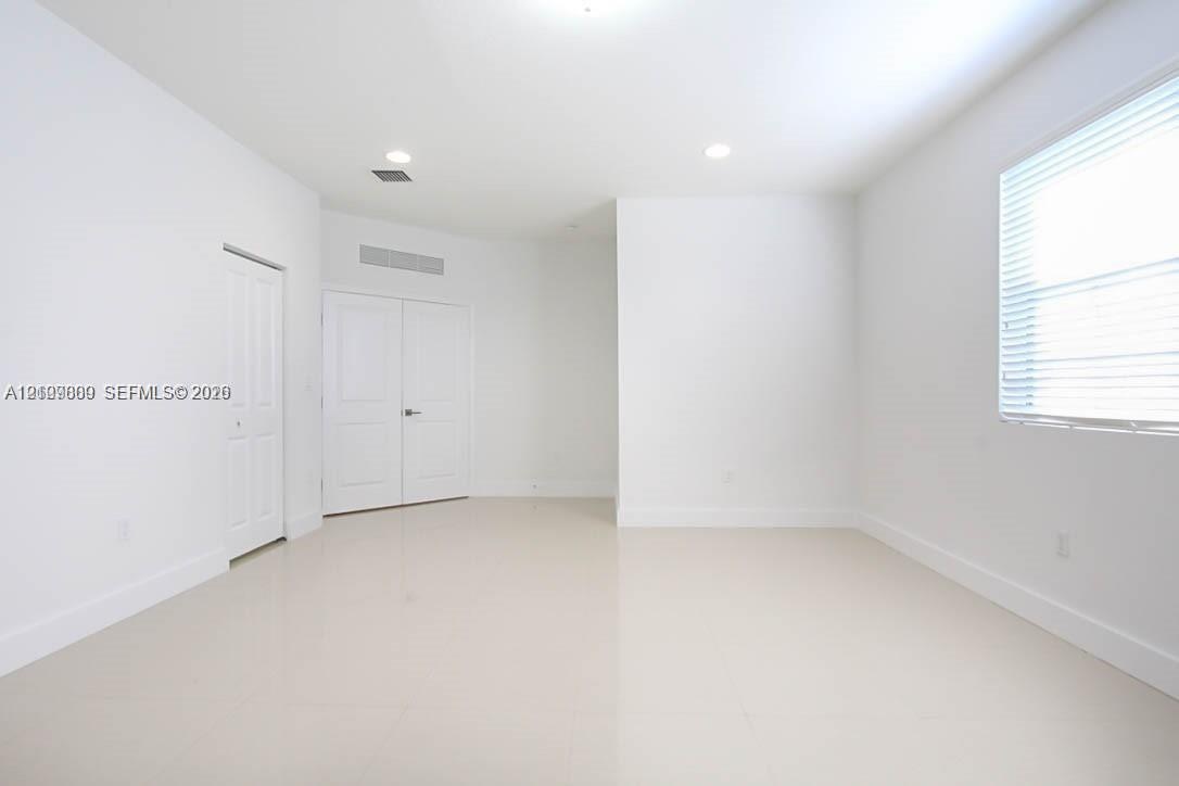 Interior space featuring neutral tile flooring, recessed ceiling lighting, a multi-pane window with horizontal blinds, and paneled closet doors