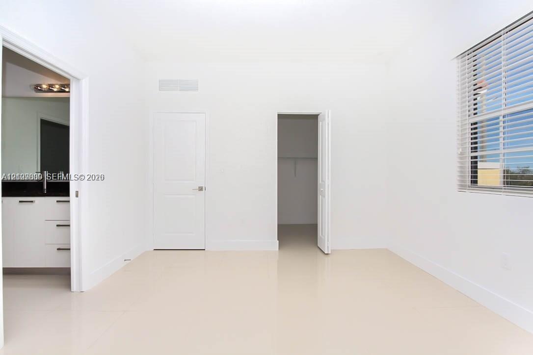 Interior room featuring neutral tile flooring, a walk-in closet with built-in shelving, a window with horizontal blinds, and access to a vanity area w