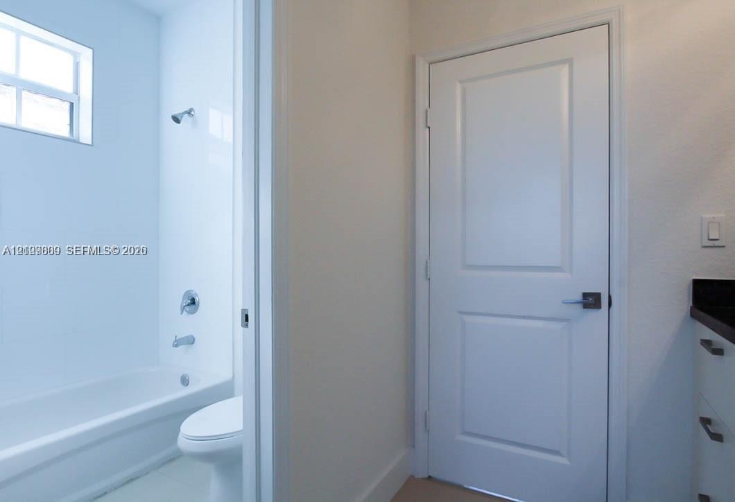 Bathroom featuring a composite bathtub with wall-mounted shower hardware, high-profile window, white shaker-style cabinetry with dark countertop, and 